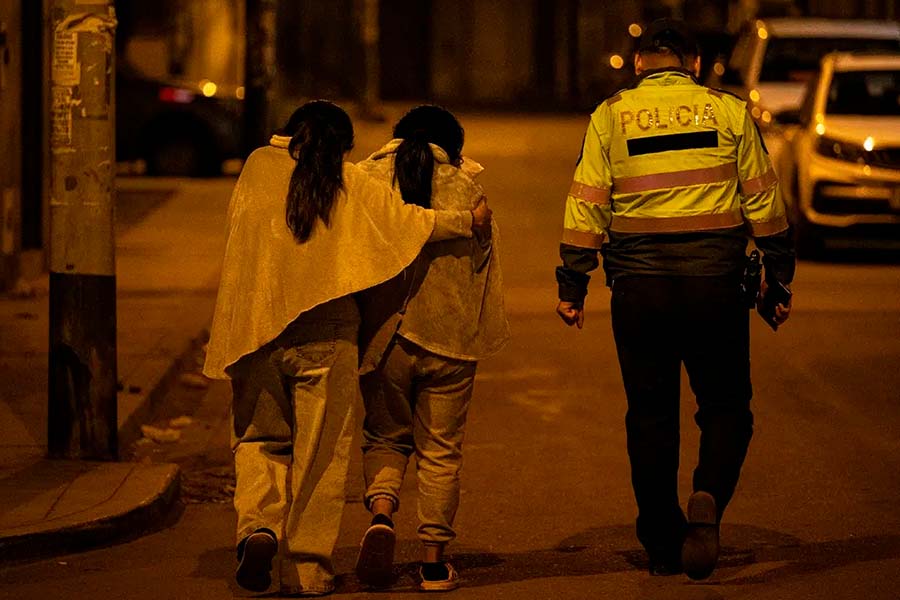 Dos niñas caminando de noche al costado de un oficial de la Policía Nacional del Perú.