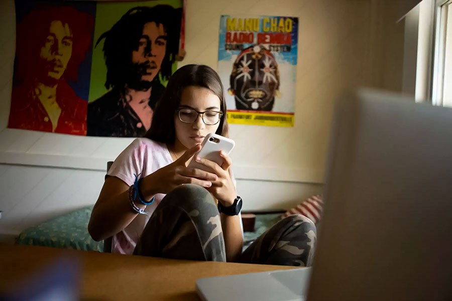 Chica joven en su cuarto viendo su celular.