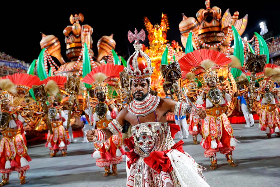 Un danzante del Carnaval de Brasil con su vestimenta típica y su grupo de baile detrás.