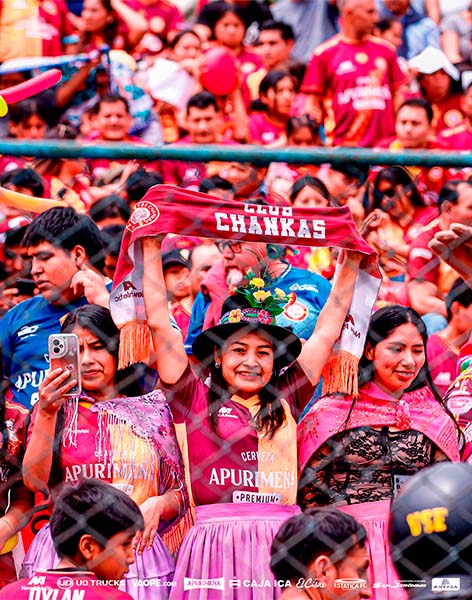 Joven fanática de Los Chankas CYC levantando una banderola del club desde la tribuna de un estadio de fútbol.
