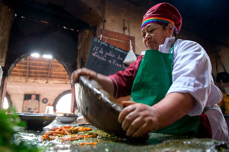 Una señora picantera peruana utilizando un batán para moler especias mientras cocina.
